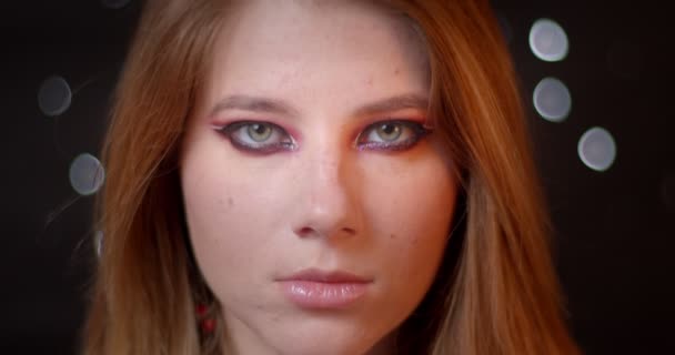 Szőke modell rendkívüli fényes make-up figyeli a kamerát, hogy nyugodt a homályos fények bokeh háttér. — Stock videók