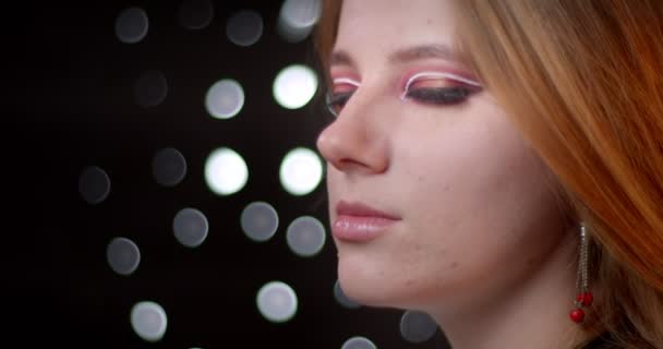 Profil shoot av Ginger modell med modern make-up vänder sig till kameran och ler positivt på bokeh bakgrund. — Stockvideo