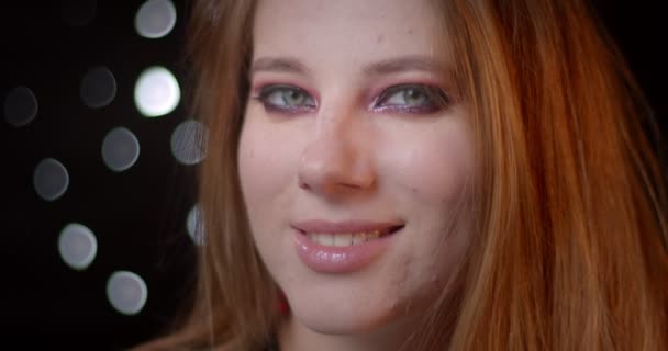 Portret van mooie blonde model met heldere make-up kijken in de camera met mysterieuze glimlach op bokeh achtergrond. — Stockvideo