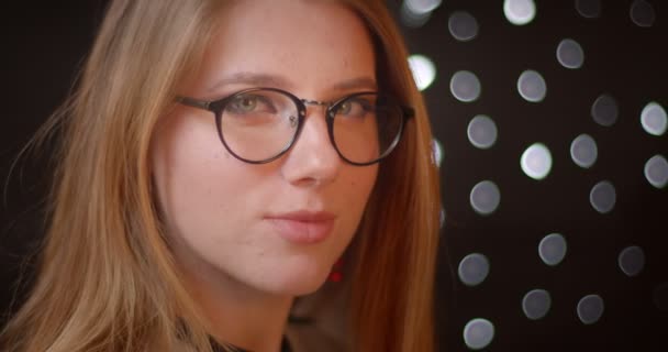 Modèle blond sérieux dans des lunettes avec un maquillage lumineux se transforme en caméra et se brise en sourire sur fond bokeh . — Video