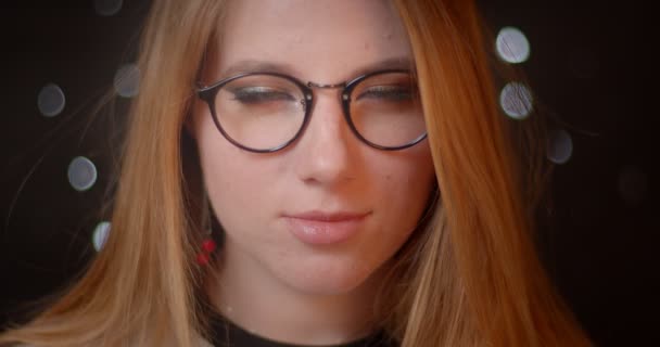 Modèle blonde avec maquillage lumineux fixe ses lunettes flirter avec la caméra sur fond bokeh . — Video