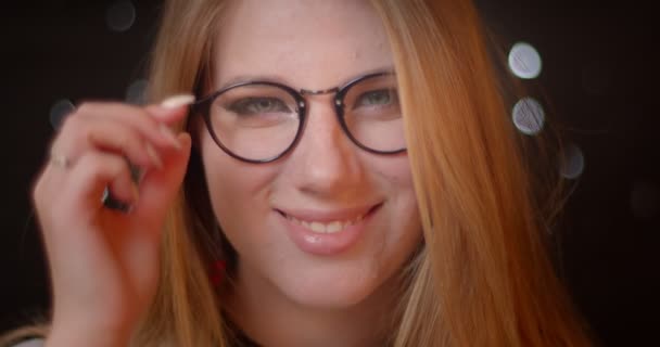 Blond model met heldere make-up corrigeert haar oog-bril kijken vreugdevol in de camera op bokeh achtergrond. — Stockvideo