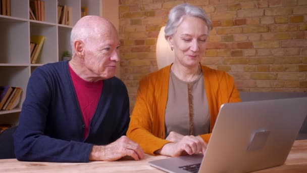 Deux hauts collègues caucasiens aux cheveux gris parlant en vidéochat sur ordinateur portable étant joyeux au bureau . — Video