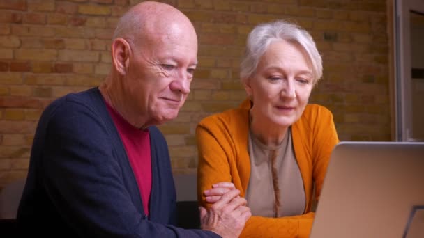 Dois cônjuges caucasianos de cabelos grisalhos idosos comunicam-se no videochat no computador portátil abraçando ternamente um a outro . — Vídeo de Stock
