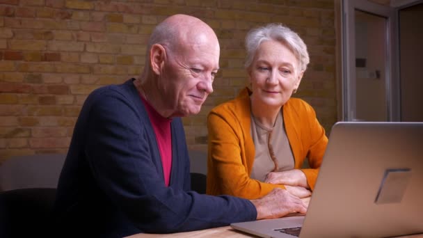 Dos ancianos de pelo gris caucásicos cónyuges hablan en videochat en el ordenador portátil de estar interesados y activos entre sí . — Vídeos de Stock