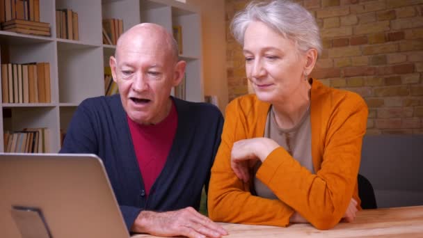 两位白发苍苍的白种人配偶的特写镜头在笔记本电脑上的视频聊天中主动在办公室里打手势. — 图库视频影像
