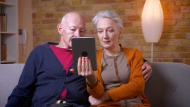 Üst düzey beyaz eşler tablette film izliyor ve oturma odasında kanepede oturan disussing.