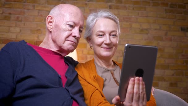 Les conjoints caucasiens aînés regardant le film sur tablette et en discutant étant intéressé au canapé dans le salon . — Video