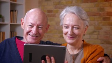 Üst düzey gri saçlı kafkas çift rahat evde tablet arkadaşları ile online videocall sahip.