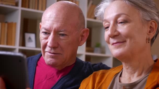 Профиль съемки старшей кавказской пары беседуют в онлайн-видеочате со своими друзьями на планшете, смеясь над уютным домом . — стоковое видео
