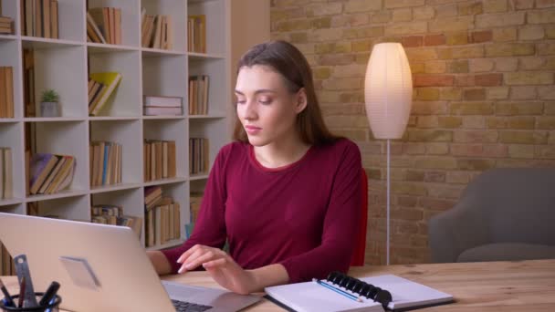Jeune femme d'affaires brune aux cheveux longs travaillant avec un ordinateur portable et un ordinateur portable attentif au bureau . — Video