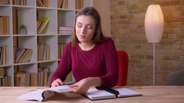 Ung brunett långhårig kvinnlig student läsa bok och göra anteckningar att vara uppmärksam i ämbetet. — Stockvideo