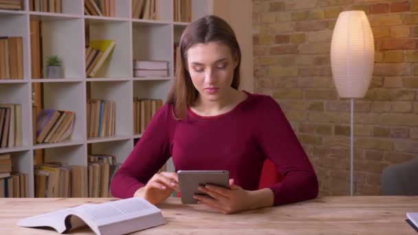 Giovane donna d'affari bruna che lavora con tablet e libro essendo attenta in ufficio . — Video Stock