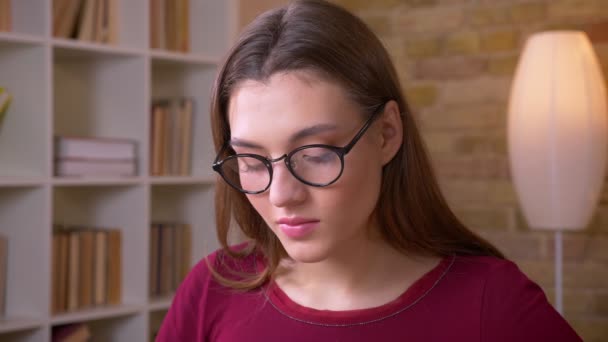 Close-up portrait of young brunette long-haired female student in eye glasses watches calmly into camera. — Stock Video