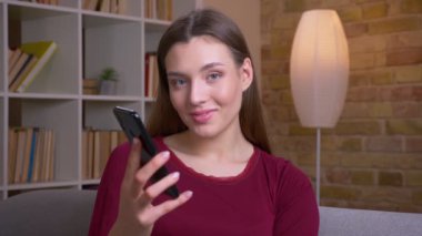 Young joyful brunette female shows upright green chroma screen of phone recommending the app at home.