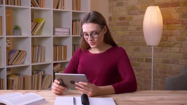 Joven y hermosa mujer de negocios morena en gafas para los ojos trabajando con la tableta siendo alegre en la oficina . — Vídeos de Stock