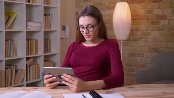 Jovem e bela mulher de negócios morena em óculos de olho jogando jogo no tablet sendo alegre no escritório . — Vídeo de Stock