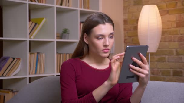 Jong en mooi brunette vrouwelijke freelancer werken met tablet wordt geconcentreerd en geïnteresseerd in thuis. — Stockvideo