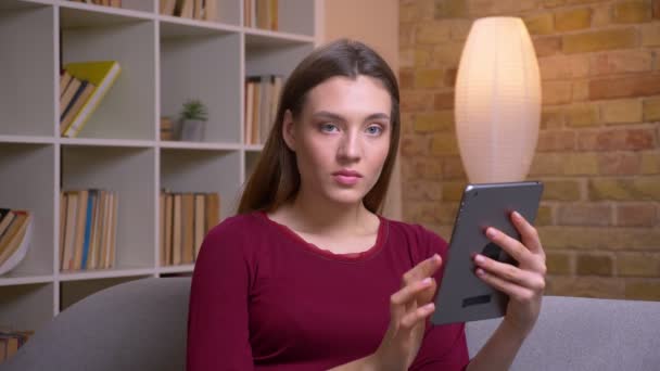 Jong en mooi brunette vrouwelijke freelancer werken met tablet draait om camera en glimlacht thuis. — Stockvideo