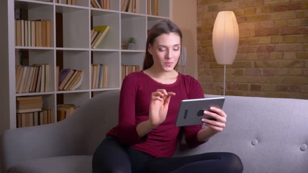 Jovem e bela morena feminina joga jogo no tablet estar interessado em casa . — Vídeo de Stock