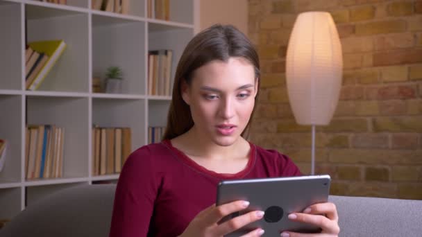 Jong en mooi brunette vrouw speelt spel op tablet wordt zeer vreugdevol thuis. — Stockvideo