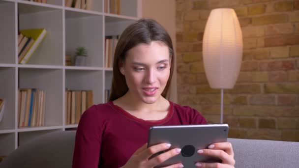 Fiatal és gyönyörű barna nő játszik játék tabletta, hogy rendkívül örömteli fordul a kamera és mosolyog otthon. — Stock videók