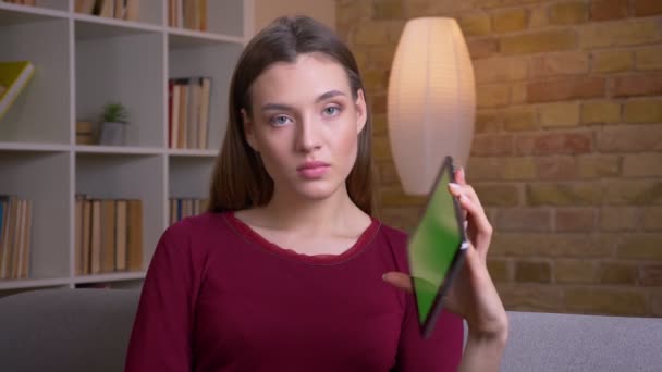 年轻美丽的黑发女性将绿色的平板电脑显示屏放入相机中，在家里推荐应用程序. — 图库视频影像
