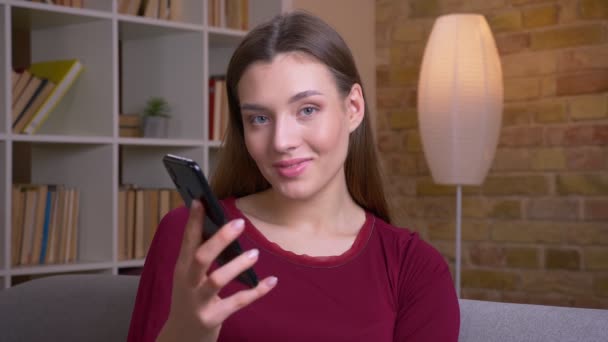 Молода радісна брюнетка жінка показує вертикально зелений екран телефону, що рекомендує додаток вдома . — стокове відео