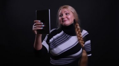 Siyah üzerine izole edilmiş arka planlı tablette görüntülü arama yaptıran orta yaşlı beyaz kadın yakın çekim portresi