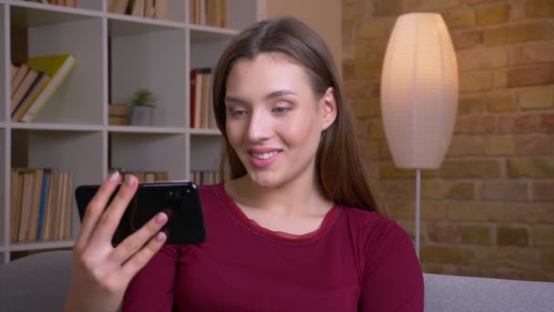 Young joyful brunette female shows upright horizontal green chroma screen of phone recommending the app at home. — Stockvideo