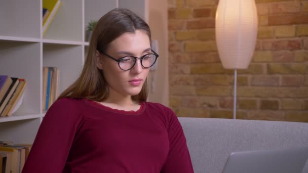 Primer plano retrato de la guapa morena freelancer femenina en gafas de trabajo con portátil sonríe en la cámara en casa . — Vídeos de Stock