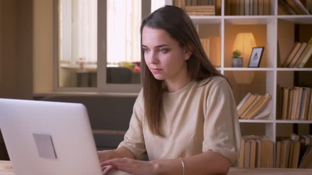Портрет крупным планом молодой привлекательной кавказской предпринимательницы, использующей ноутбук в помещении офиса — стоковое видео
