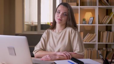 Genç başarılı ve başarılı beyaz iş kadınının kameraya bakıp ofisteki dizüstü bilgisayarı kullanarak gülümseyen yakın çekim portresi