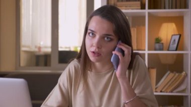 Ofiste dizüstü bilgisayar üzerinde çalışan bir telefon görüşmesi olan genç çekici beyaz iş kadını Closeup portre