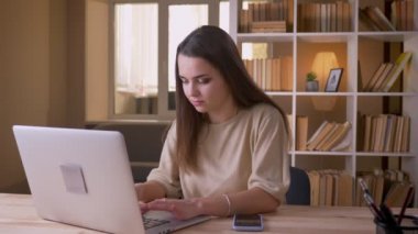 Dizüstü bilgisayarı kullanan ve ofiste ki telefonda heyecan verici bir bildirim alan genç mutlu beyaz iş kadınının yakın çekim portresi