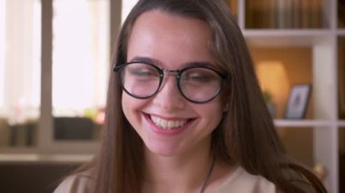 Genç çekici beyaz kız öğrencinin gözlüklü yakın çekim portresi kameraya bakarak gülümseyerek ve daire nin içinde mutlu bir şekilde gülüyor