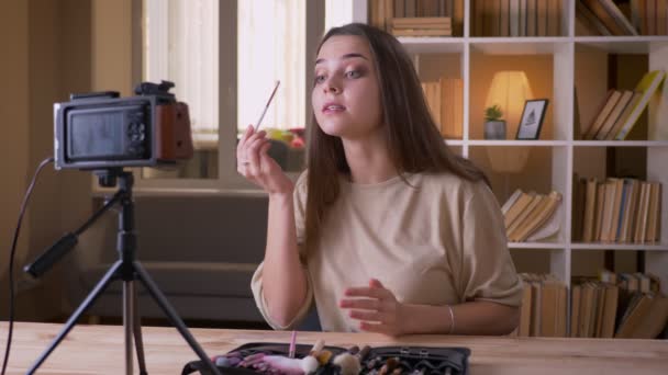 Retrato de close-up do jovem atraente blogueiro de beleza feminina caucasiano falando na câmera e fazendo uma revisão do produto dentro de casa — Vídeo de Stock