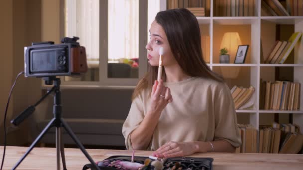 Closeup portrait of young attractive caucasian female beauty blogger talking on camera and making a product review in the apartment indoors — Stock Video