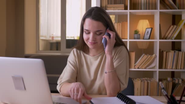 Closeup portré fiatal vonzó kaukázusi üzletasszony, amelyek a telefonhívás segítségével a laptop beltéri az irodában — Stock videók