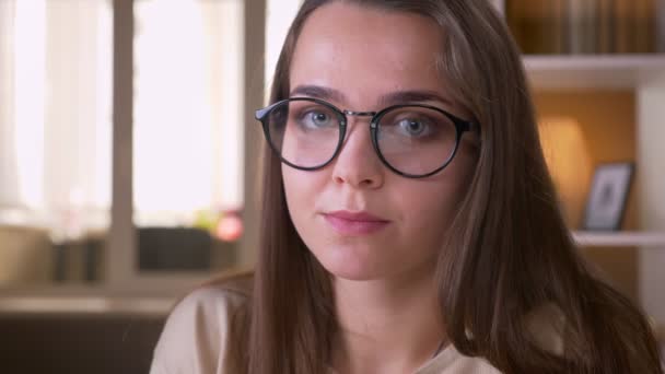 Primer plano retrato de joven atractiva estudiante caucásica en gafas mirando a la cámara sonriendo felizmente en el interior del apartamento — Vídeo de stock