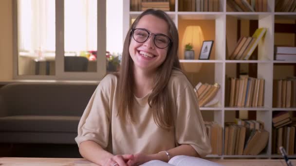 Gros plan portrait de jeune étudiante caucasienne attrayante dans des lunettes regardant la caméra rire joyeusement à l'intérieur dans la bibliothèque du collège — Video