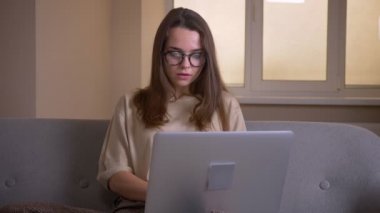 Kapalı kanepede oturan dizüstü bilgisayarda yazarak gözlük genç çekici kafkas iş kadını Closeup portre