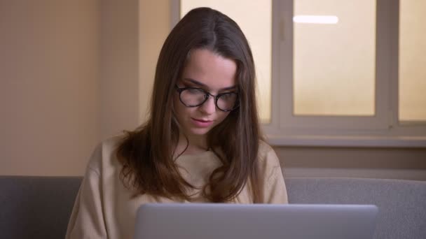 Nahaufnahme Porträt der jungen attraktiven kaukasischen Geschäftsfrau mit Brille tippt auf dem Laptop drinnen im Büro — Stockvideo