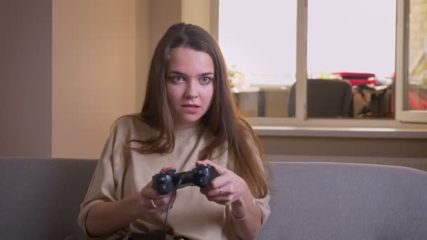 Nahaufnahme Porträt einer jungen attraktiven kaukasischen Frau, die glücklich auf der Couch in der Wohnung sitzt und Videospiele spielt — Stockvideo