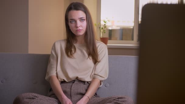 Närbild porträtt av unga attraktiva kaukasiska kvinna tittar på TV sitter på soffan är avslappnad inomhus i lägenheten — Stockvideo