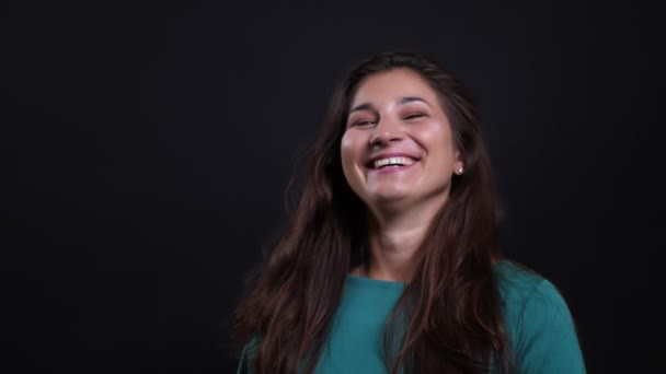 Close-up retrato de jovem morena bonita fêmea sorrindo e rindo alegremente olhando para a câmera com fundo isolado no preto — Vídeo de Stock