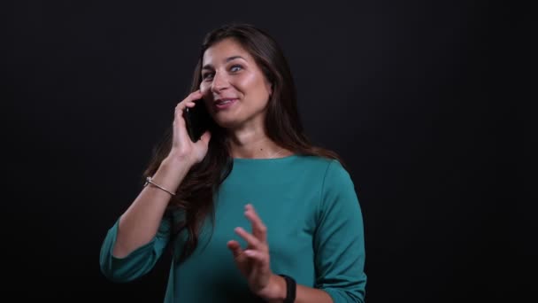 Close-up retrato de jovem bonita morena feminino ter um telefonema olhando para a câmera com fundo isolado no preto — Vídeo de Stock