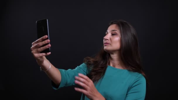 Портрет крупным планом молодой красивой брюнетки женщины, делающей селфи по телефону на фоне, изолированном от черного — стоковое видео