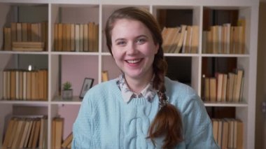 Üniversite kütüphanesinde kameraya bakarak gülümseyen bir kitap okuyan genç güzel kız öğrencinin closeup portrekapalı