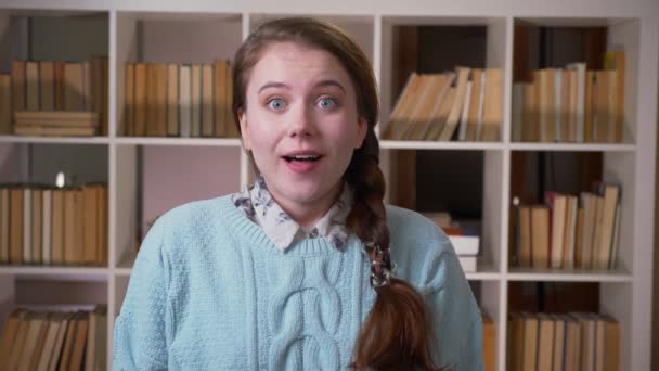 Nahaufnahme Porträt einer jungen hübschen Studentin, die aufgeregt und glücklich in die Kamera in der Universitätsbibliothek blickt — Stockvideo